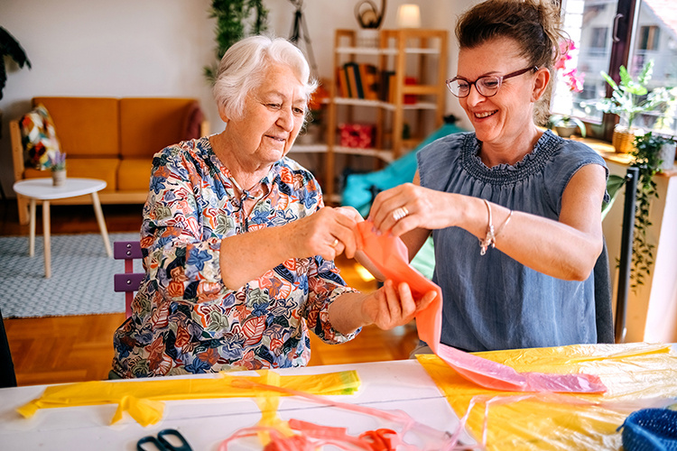 Two senior women working at table creating artwork with cloth