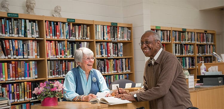 Senior woman and man standing at a counter in surrounded by library bookshelves