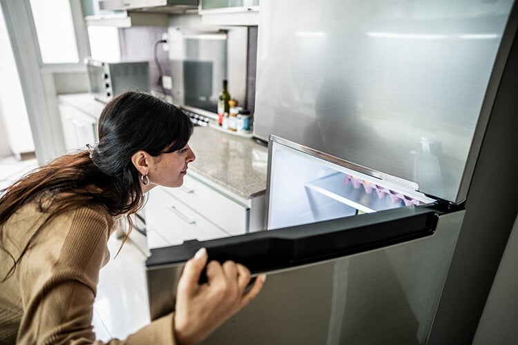 Woman checking open refrigerator for food 