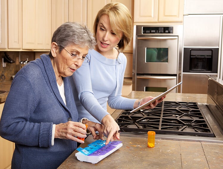 Adult woman helping elderly woman organize medications