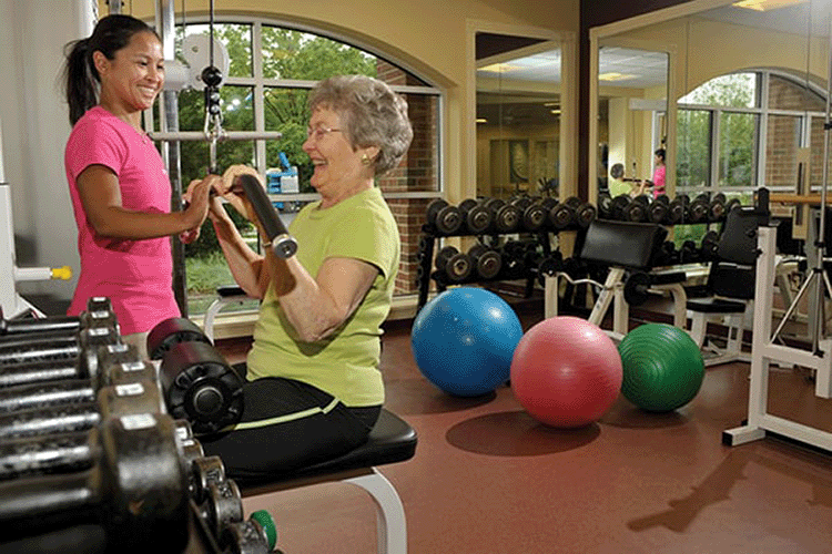 Senior retired woman working weight machine with assistance