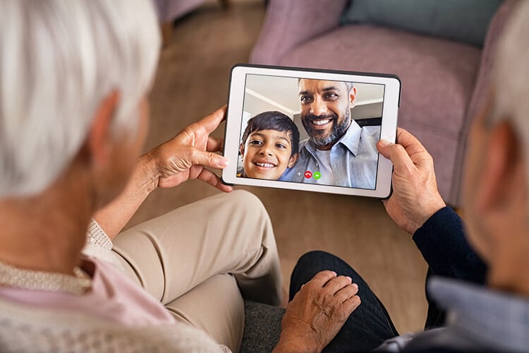 Two seniors using tablet to chat with grandson and son