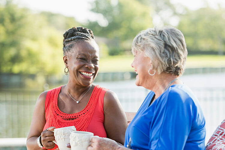 Two senior friends chatting and smiling with coffee cups