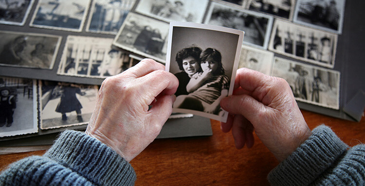 Older person hands holding a back and white photos with photo albums in the background