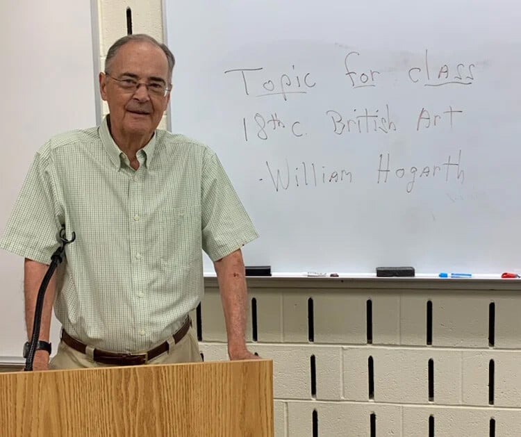 Senior man at a podium in front of a white board teaching a lifelong learning class