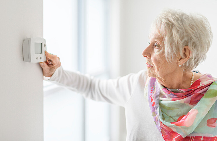 Senior woman adjusting thermostat for holiday travel